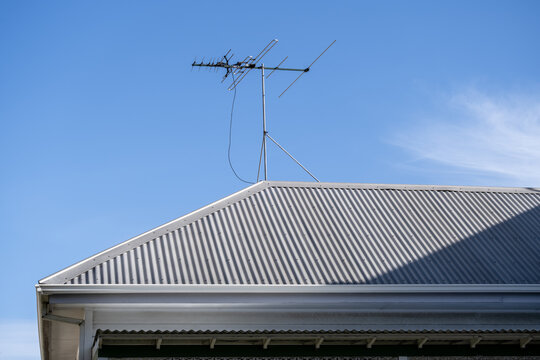 Television antenna mounted on top of a corrugated metal roof of a residential suburban house&nbsp;against a clear blue sky in Australia. Concepts of signal reception, domestic housing, media transmission
