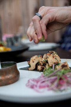Male hand squeezing lime over chicken chunks with onions in the foreground, selective focus 