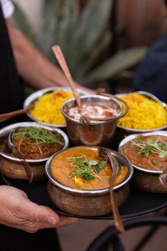 high angle shot of waiter carrying tray of indian curries and side dishes and saffron rice in silver bowls