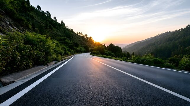 A winding asphalt road curves through lush green hills under a soft golden sunset sky with distant mountain ridges