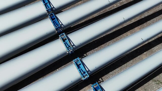 blue lifting equipment transporting white wind turbine blades in industrial setting