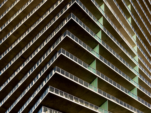 Tight architectural composition of a contemporary high-rise residential building corner, showing multiple levels of cantilevered concrete balconies with glass railings.