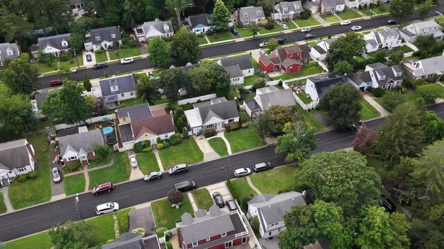 Rows of West Hempstead houses and lawns extend beside local streets, Nassau County on Long Island, New York. The aerial camera travels east at nearly level altitude. The landscape is seen in daylight.