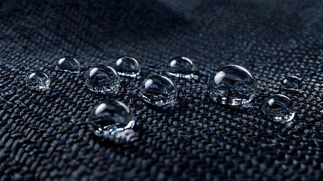 Close-up of water droplets beading on surface of dark water-repellent technical fabric textile material