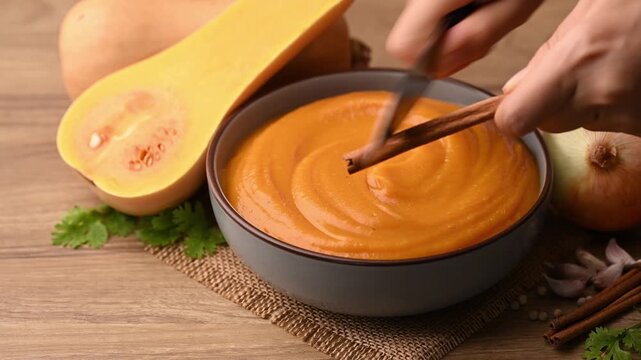 Hands grating a cinnamon stick over a bowl of creamy butternut squash soup for garnish, homemade food in autumn