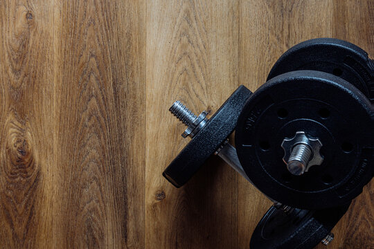 Black adjustable dumbbells and weight plates on a wooden floor background with copy space for fitness training design. Horizontal format