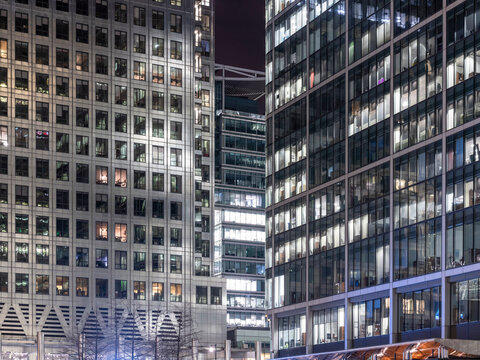 Nighttime view of multiple glass and stone office towers in London's Canary Wharf financial district.