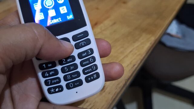 Close up of a person using vintage feature phone with physical keypad and screen showing inbox menu over wooden table background