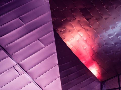 Close-up of faceted metal panel cladding on a building exterior, where multiple planes converge at sharp diagonal ridges. 
