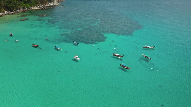 Longtail boats floating on turquoise water near shore of tropical beach in Phuket, Thailand, vibrant marine life and clear ocean during a sunny day. Summer travel vacation. Rise up drone aerial shot