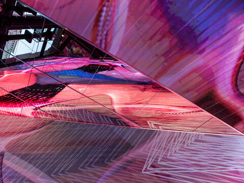 Close-up of an angled glass architectural surface reflecting a saturated abstract composition of pink, red, and blue light patterns.