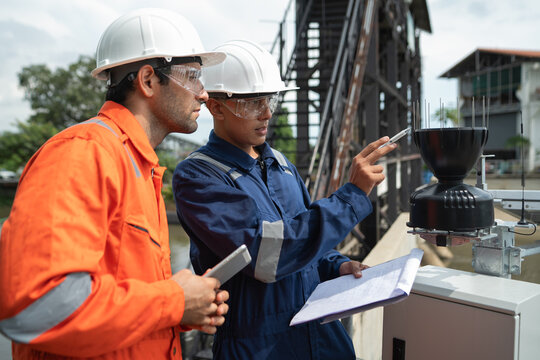 Engineers check environmental monitoring sensor and review technical documents during inspection of water management infrastructure.