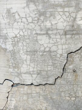 Close-up of a weathered concrete wall showing rough texture and deep cracks, providing an abstract background with ample copy space for design.