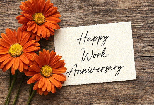 Bright orange flowers beside work anniversary greeting card on rustic wooden surface