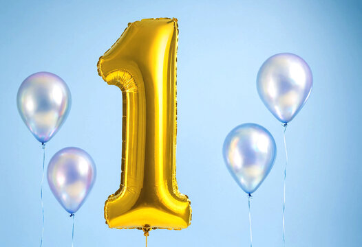 Golden number one balloon surrounded by pastel colored balloons against sky