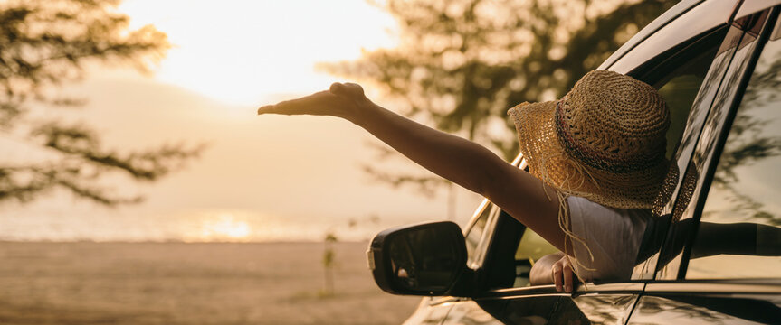 Woman wearing straw hat sits in front seat waving hand out car window at sunset feeling the wind. Happy weekend travel enjoy summer at beach. summer vacation travel driving road trip