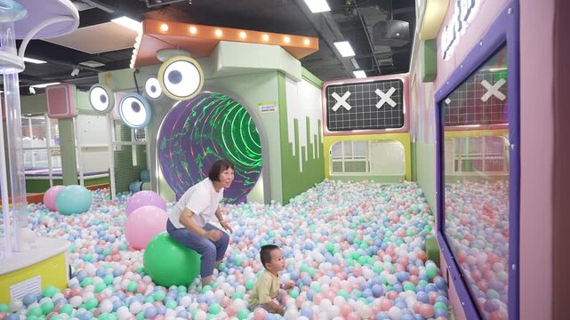 Wide shot of grandmother and toddler playing in indoor ball pit