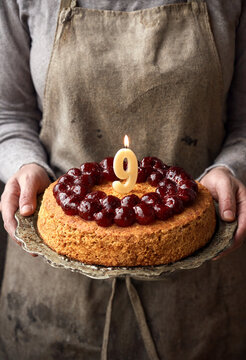 Person holding birthday cake with lit candle and berry topping