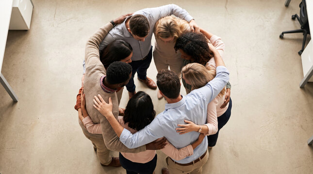 Coworkers sharing group hug in office showing teamwork and support with diverse people standing in circle
