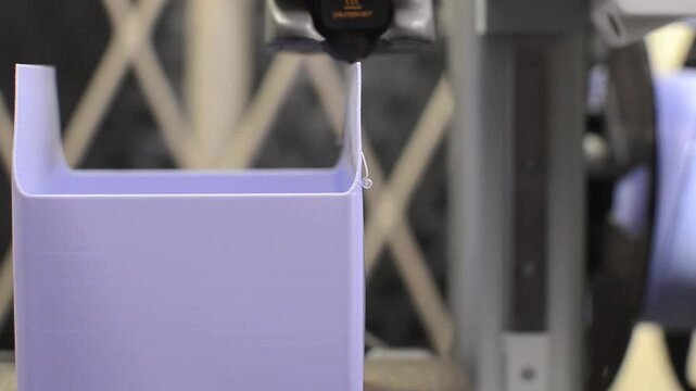3D printer extruder nozzle printing a purple plastic object layer by layer in extreme close up shot