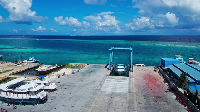 High angle drone perspective of island shipyard facility, dry dock, and boats on land under cloudy sky. Ideal visual asset for marine logistics and industrial guides.Himmafushi.Maldives