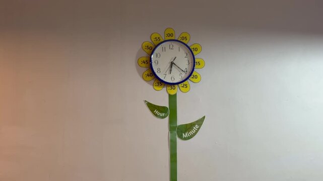 Educational wall clock designed as a sunflower, with yellow petals labeled in five-minute increments and leaves marked "Hour" and "Minute" to help children learn to tell time.