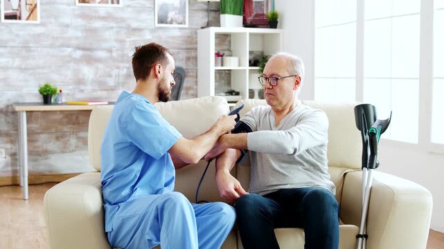 Male nurse measures blood pressure on an older man in a bright care setting, providing routine health monitoring and supportive senior healthcare, also emphasizing prevention and assessment.