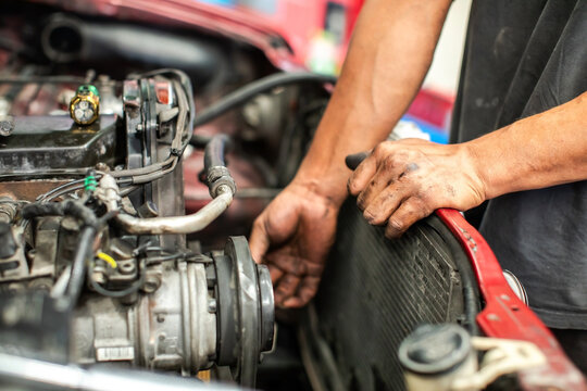 Close-up of a mechanic's hands repairing a car engine and radiator at an auto service garage. Concept of vehicle maintenance, inspection, and repair.