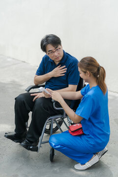 Nurse in blue scrubs checking temperature with infrared thermometer for senior male patient in wheelchair.