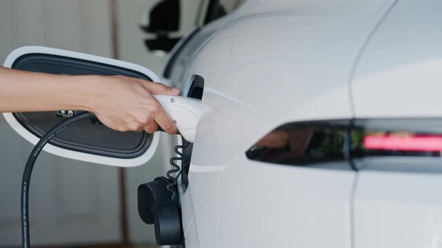 Person plugging in EV charging cable to white electric vehicle for sustainable energy transport.	