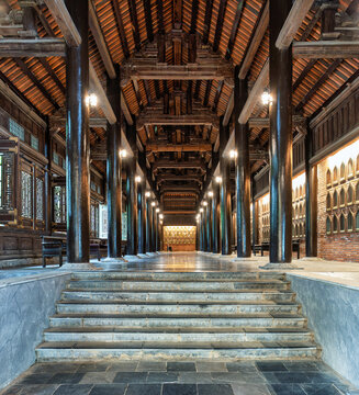 Perspective view of the traditional wooden Arhat Corridor at Bai Dinh Pagoda in Ninh Binh, Vietnam, showcasing historical Buddhist architecture and ornate pillars