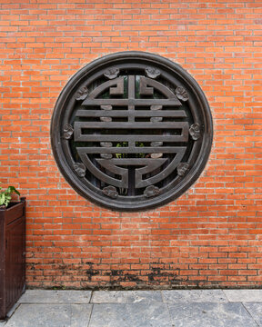 Traditional circular lattice window with a Shou symbol set into an orange brick wall at the Bai Dinh Temple in Ninh Binh, Vietnam