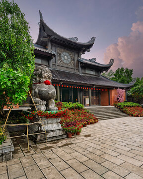 Stone lion at Bai Dinh Pagoda, Ninh Binh, Vietnam, featuring traditional wooden architecture and colorful flowers in a stone courtyard at sunset