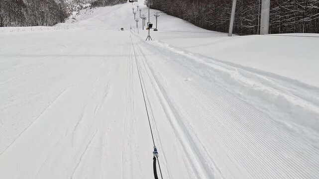 美しい圧雪バーンを滑走式リフトで登るスキーヤーの足元主観映像（POV）