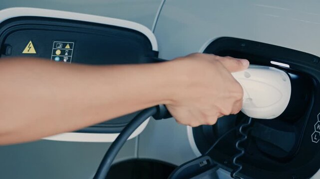 Person plugging in EV charging cable to white electric vehicle for sustainable energy transport.	