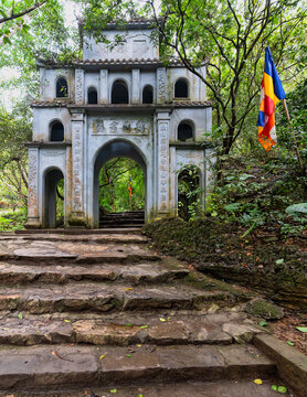Stone steps leading to an ancient arched gateway in the Bai Dinh Pagoda complex, surrounded by lush forest trees in Ninh Binh, Vietnam