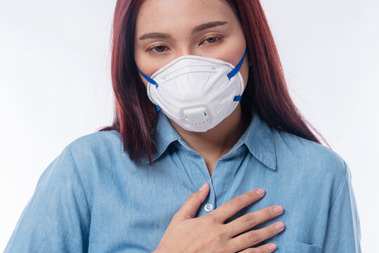 Stressed young Asian woman wearing N95 protective face mask holding hand on chest having breathing difficulty isolated on white background. Air pollution PM2.5 and respiratory disease health concept.