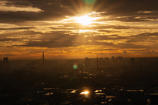 Majestic golden sunset over Bangkok city skyline silhouette with bright sun rays piercing through dramatic clouds. Urban metropolis architecture background with lens flare and copy space.