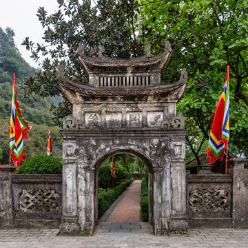 Stone gate with traditional architecture and ceremonial flags at the Temple of Emperor Dinh Tien Hoang in Ninh Binh, Vietnam