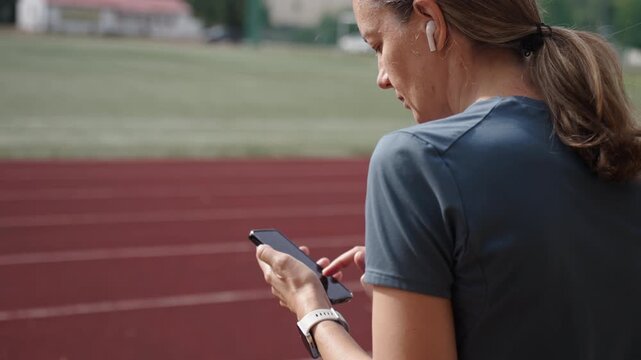 Woman using smartphone before running on stadium track