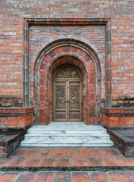 Intricate wooden door entrance at Bai Dinh Pagoda tower, Ninh Binh, Vietnam, featuring traditional architecture with red brick walls, stone carvings, and marble steps in a Buddhist temple complex