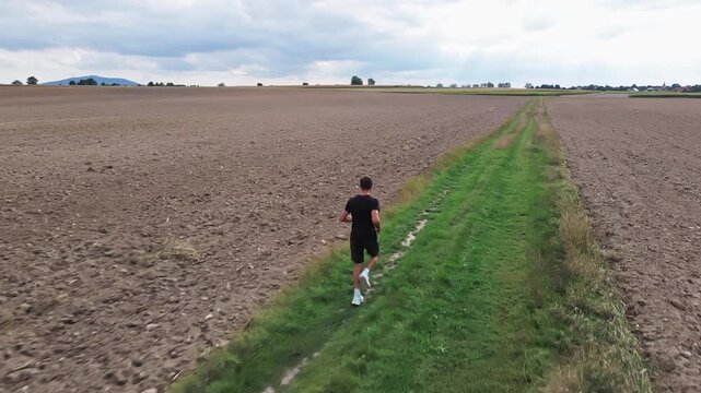 Man running along a grassy path between plowed fields in the countryside