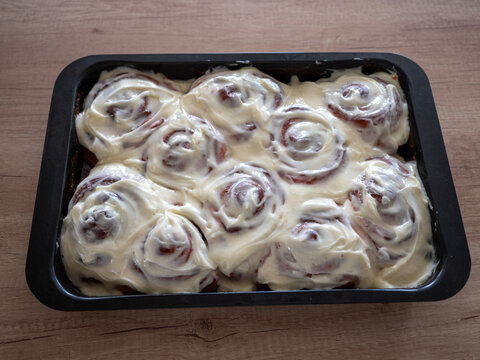 Homemade cinnamon buns covered with rich creamy frosting in a baking pan, featuring classic spiral shapes and soft sweet dough, ideal for bakery, dessert, breakfast and home baking concepts.