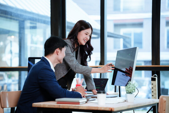 Asian financial professionals discussing investment strategies and market trends while reviewing stock charts and financial data in a modern office.