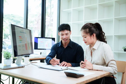 Asian business professionals collaborating on a creative project, discussing ideas and reviewing work on a computer in a modern office.