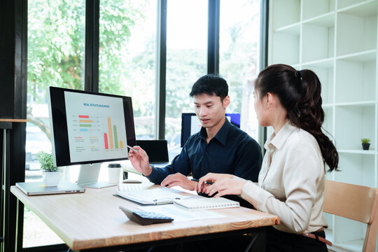 Asian business professionals collaborating on a creative project, discussing ideas and reviewing work on a computer in a modern office.