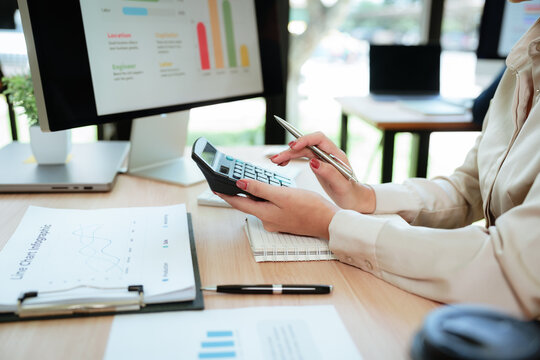 Asian businesswoman analyzing financial data and business charts while taking notes and reviewing reports at a modern office desk.