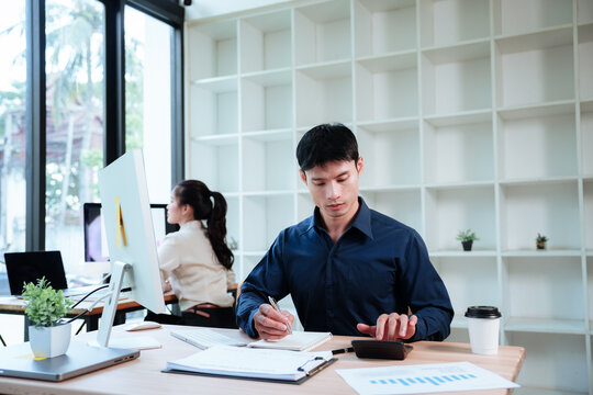 Asian business professionals working independently in a modern office, using computers to analyze sales data, reports, and business performance.