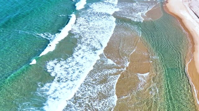 Aerial top-down view of beautiful emerald ocean waves breaking on a white sand beach in South Korea.