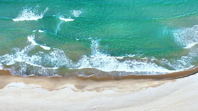 Aerial top-down view of beautiful emerald ocean waves breaking on a white sand beach in South Korea.